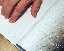 An open notebook containing notes written in braille, and a hand whose fingers are touching them.