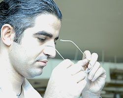 A profile head shot of a man getting ready to put on a pair of glasses, which he holds in his hands.