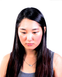 A young woman with long black hair, facing the viewer but looking downwards, appearing to be distraught.