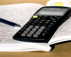 A black calculator and black pen lying on top of an open notebook.