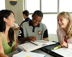 Two young women and a young man sitting around a table in a study group. School books are open in front of them, and they are laughing and talking.