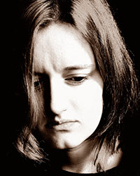 A black and white photo of a young woman looking downcast.