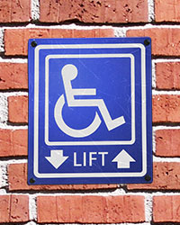 A blue-and-white wheelchair lift sign on a brick wall.