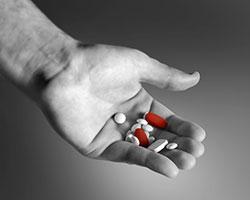 A black and white picture of an open hand holding about 10 pills of different shapes and sizes, two of which are red.