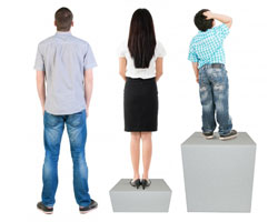 Three people, backs to us, are looking over a fence. The tall man is standing on the ground. A woman, shorter than the man, is standing on a short riser, so her head is the same height as the mans. A child is standing on top of a high riser, so his or her head is at the same height as the others.
